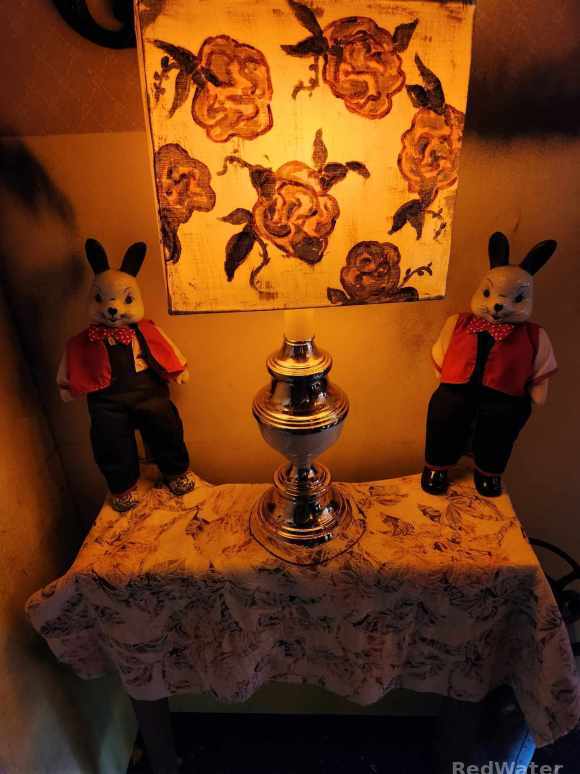 Two rabbit dolls with sinister faces and human-like figures sit on a small table