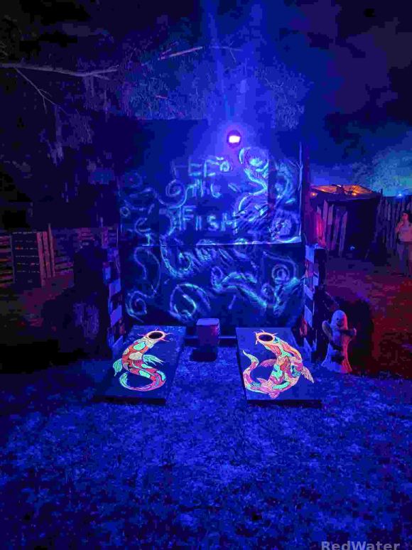 two corn hole boards are visible in the dark, evident by the glowing koi fish pattern on them