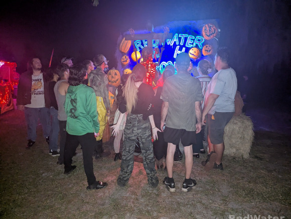 Several people gathered around a creepy skull photo op with their back to the camera and their hands all extended out to the side