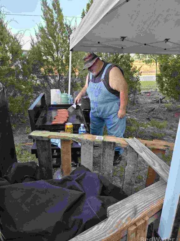 a man in overalls stands over a grill